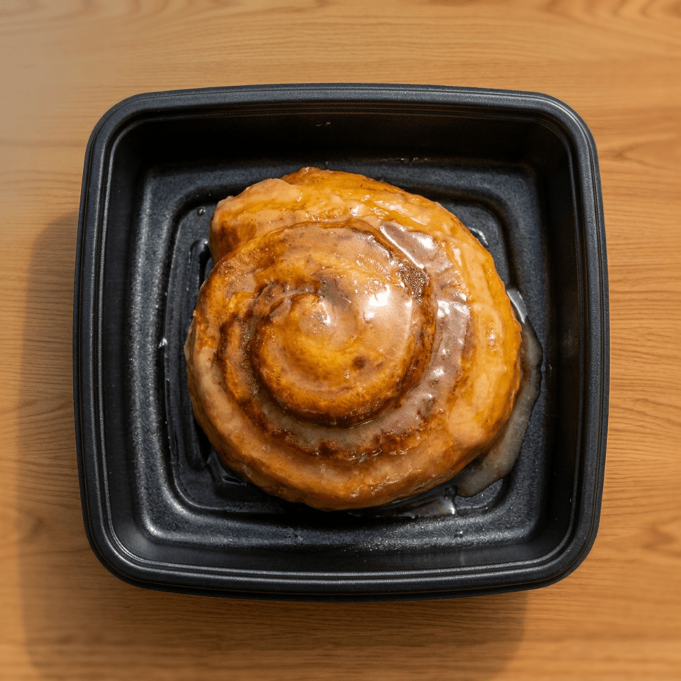Glazed cinnamon roll served in a black rectangular dish on a wooden table.