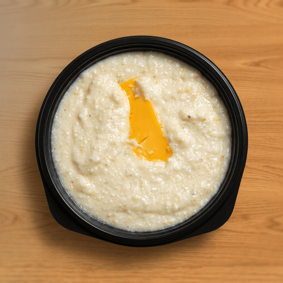 Creamy mashed potatoes topped with a pat of melting butter in a black bowl on a wooden table.